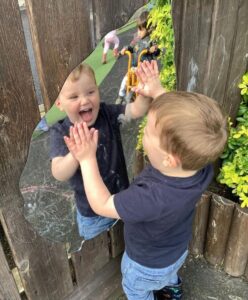 toddler laughing looking at his own reflection in a mirror